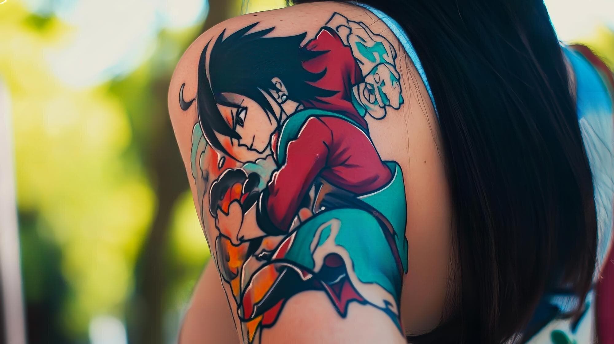 Vibrant anime-style color tattoo on woman's shoulder and back showing bold red teal and orange ink before laser color removal